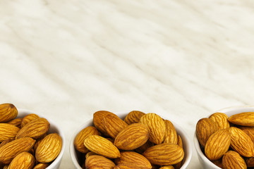 Three white bowls with almonds stand on a white marble surface