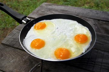 Old wooden table and frying pan with fried eggs on camping gas stove