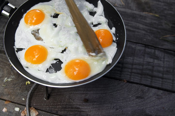 Fried eggs cooked in frying pan on camping gas stove on old wooden table