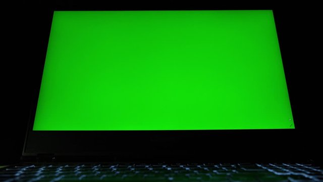 Laptop with green screen. Dark office. Close up.