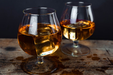 Two whiskey / cognac glasses with ice on a wooden background. Dark backdrop.