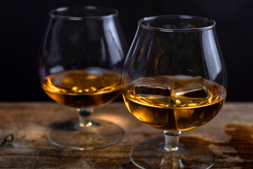 Two whiskey / cognac glasses with ice on a wooden background. Dark backdrop.