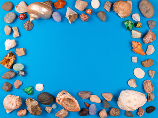 Photo frame of sea shells and pebble on bright blue background with space for your text or photo