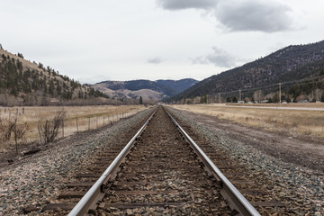 Empty railroad track leading to vast tree covered rolling hills on overcast day