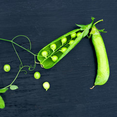 Fresh green pea pods on a black surface, top view