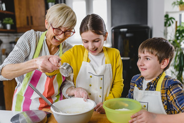 Grandmother and her grandchildren making cakes together in the home kitchen. Children helping...