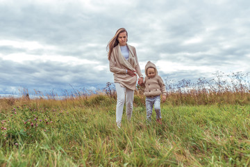 Woman mom walks with her child, autumn day in the park, background field, strong wind, clouds, free space for copy text. Walk in the countryside in nature. Casual warm clothes.