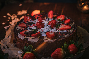 Vegan and raw chocolate cake with strawberries, cocnut flakes and raspberry seeds, served on a paper serviette in a soft light of a restaurant, haute cuisine, view from the side and close up