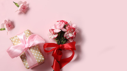 Carnations with a gift on a pink table, abstract spring floral background. Creative modern bouquet, minimal holiday concept. Greeting card for Women's Day or Mother's Day, happy birthday, wedding, 