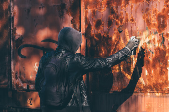 Homeless man spray painting old train wagon with aerosol can