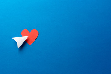 Paper plane with red heart shape on blue background with space for text. Sharing and send concept.