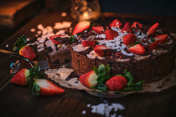 Vegan and raw chocolate cake with strawberries, cocnut flakes and raspberry seeds, served on a paper serviette in a soft light of a restaurant, haute cuisine, view from the top and close up