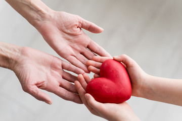 Childs hands and older woman hands holding heart. Concept o love, share and care. Care for elderly concept.