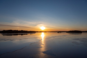 Fototapeta na wymiar Amazing winter sunset in Finland. Cold afternoon in February, reflecting water and icy surface. Wintry landscape wallpaper, copy space.