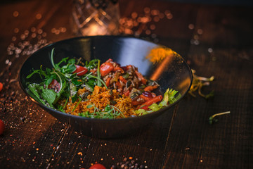 Hot, vegetarian plate of meal which includes cooked vegetarian pilaf served with healthy mix of ruccola leafs, bulgarian pepper, thin sliced vegetables, cherry tomatoes and spices, on a black