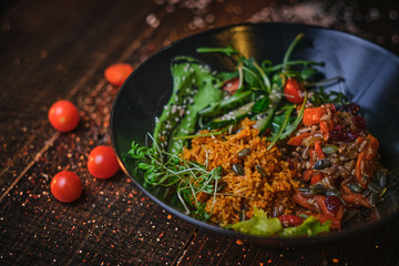 Hot, vegetarian plate of meal which includes cooked vegetarian pilaf served with healthy mix of ruccola leafs, bulgarian pepper, thin sliced vegetables, cherry tomatoes, seeds and spices, on a black