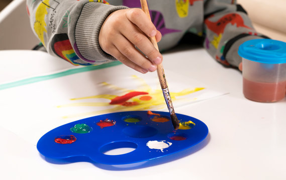 Child's hand painting yellow picture with a brush