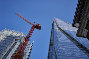 Picture of the blue sky between skyscrapers made from glass and steel in the downtown of London, capitol of Great Britain. One building is ready and second is with tall red crane to be finished soon.