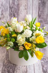  flowers with white peonies, roses, eustomas and yellow tulips, mimosa with green leaves in the papper gift box on the grey background. Spring medley bouquet. Valentine's Day. Happy Mother's Day