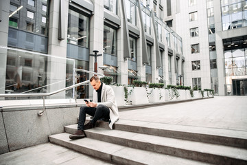 Attractive guy in casual coat sits on the steps