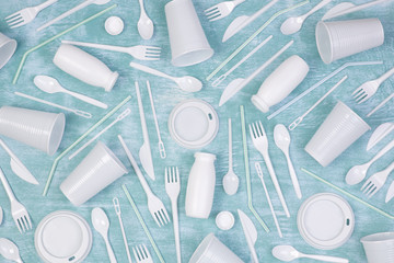 Disposable white single use plastic objects such as bottles, cups, forks and spoons  on blue background