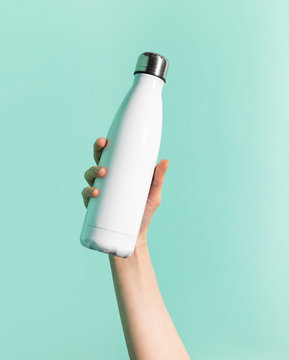 Close-up of female hand holding white reusable steel stainless thermo water bottle isolated on background of cyan, aqua menthe color. Plastic free.