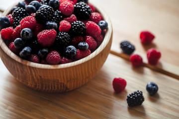 blueberries and raspberries, blackberry in a wooden bowl on old wood background