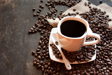 Black coffee in a white cup on the background of scattered coffee beans