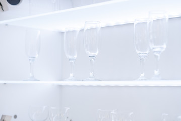 Clean wine glasses and champagne flutes upended on a white wooden shelf in a kitchen or bar