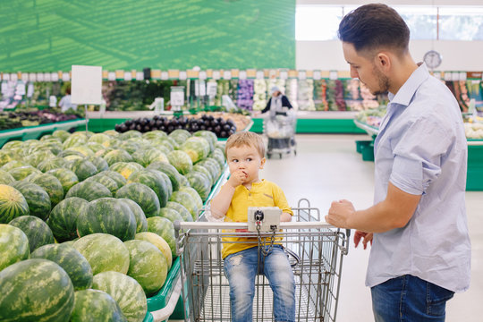 Caucasian Father Shopping In Grocery Store With Baby Son. Dad Buying Fresh Fruits For Family. Man Parent With A Toddler Kid Choosing Healthy Meal. Lifestyle Authentic Candid Moment.