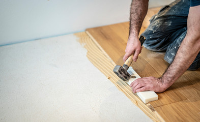 Handwerker verlegt Parkettboden und schlägt die Dielen mit dem Hammer und dem Schlagklotz zusammen