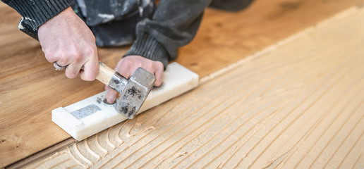 Handwerker verlegt Parkettboden und schlägt die Dielen mit dem Hammer und dem Schlagklotz zusammen