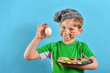 Little artist in a beret, preparing for the Easter holiday with a palette and an egg in his hand.