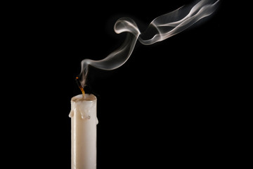 An extinguished candle on a black background, smoke goes from the wick to the top. The concept of...