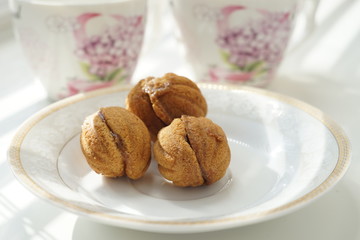 Three small cookies in the form of walnuts on a white saucer. Background two cups for tea on a sunny table