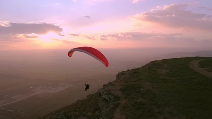 Professional paraglider float in air on parachute. Man paragliding and descending down from sky in beautiful pink sunset. Amazing adventure or activity to try new experiences - Powered by Adobe