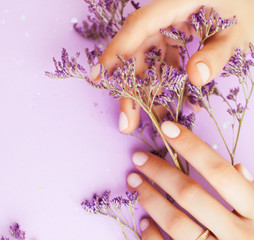 Obraz na płótnie Canvas pretty perfect woman hands with white manicure and little flowers on colorful lilac background, green leaf spa concept