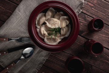 Russian traditional meal homemade dumplings in a pot with sauce, dill and drinks on a dark wooden background covered by sackcloth, national cuisine concept, top view