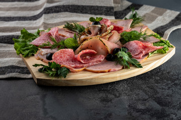 Assorted sliced delicious meat mix as salami, bacon and ham with parsley and olives on a wooden cutting board on grey cement background with tablecloth