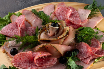 macro view assorted sliced delicious meat mix as salami, bacon and ham with parsley and olives on a wooden cutting board