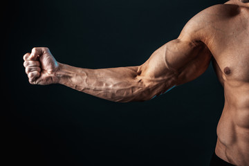 tense arm clenched into fist, veins, bodybuilder muscles on a dark background, isolate. - obrazy, fototapety, plakaty