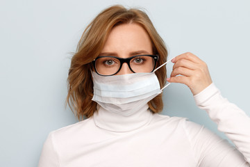 Studio portrait of woman in glasses wearing face medical mask, looking at camera, isolated on blue...