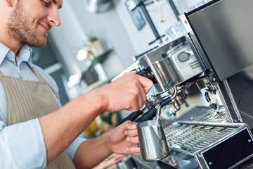 Young adult barista working in cafe, whipping milk for coffee