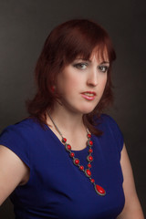 Portrait of a full grown woman, brunette, In a blue dress and red jewelry