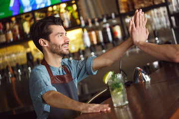 Professional Occupation. Bartender standing at counter serving mojito giving high five to customer happy