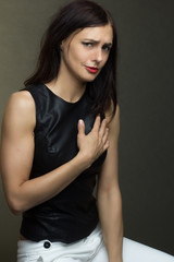 a brunette in a black leather sleeveless blouse poses on a gray background