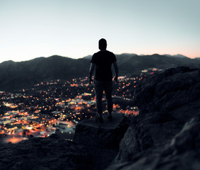 silhouette of man on top of mountain at sunset overlooking town