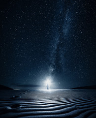 Man with flashlight walks in the sand at night under milky way