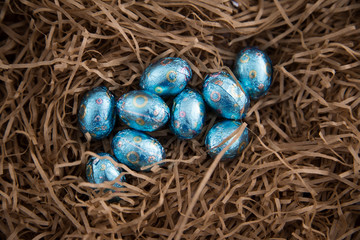 Fototapeta na wymiar Pile of small pale blue foil wrapped chocolate Easter eggs lying on top of a nest of paper straw used for packing. Looks like a child has collected in Easter hunt. Copy space. Sustainability concept. 