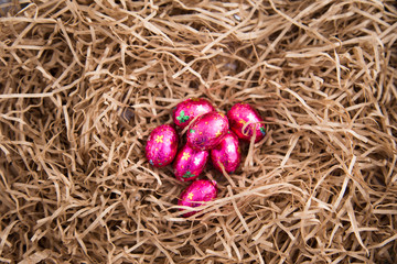 Pile of small pink foil wrapped chocolate Easter eggs lying on top of a nest of paper straw used for packing. Looks like a child has collected in Easter hunt. Copy space. Sustainability concept.